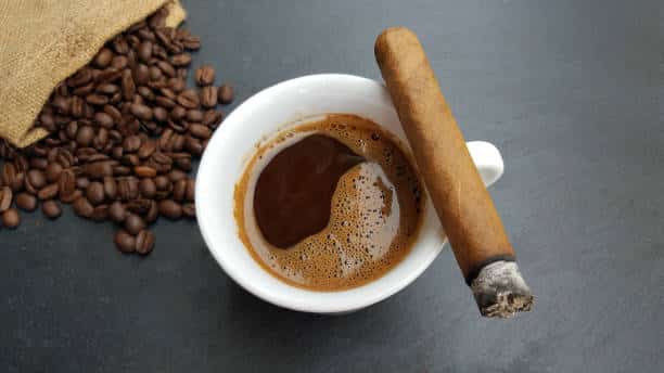 Coffee cup, beans and cigar on dark stone background