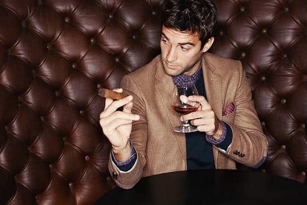A stylish man drinking whiskey and smoking a cigar
